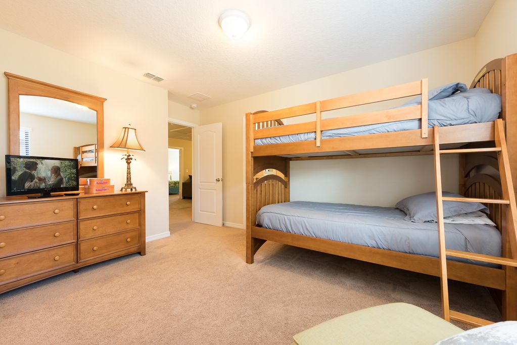 A bunk bed room with a wooden dresser, a television, and a lamp.