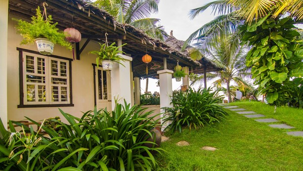 A traditional house with a thatched roof, potted plants, and a stone pathway. - VILLA SEA VIEW 1 BEDROOM (Hoi An)