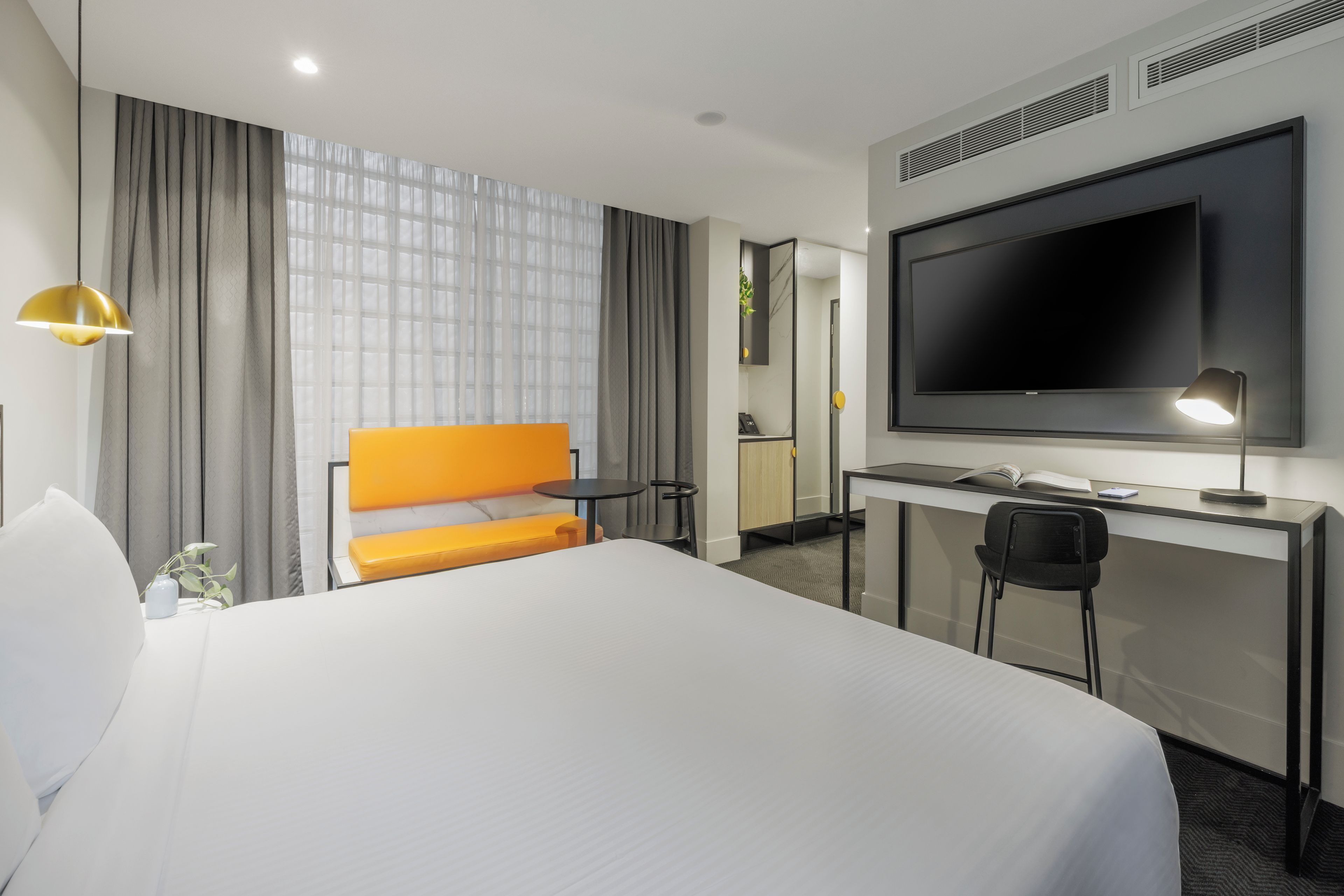 A hotel room with a large bed, a desk with a flat-screen TV, a chair, and a small table.