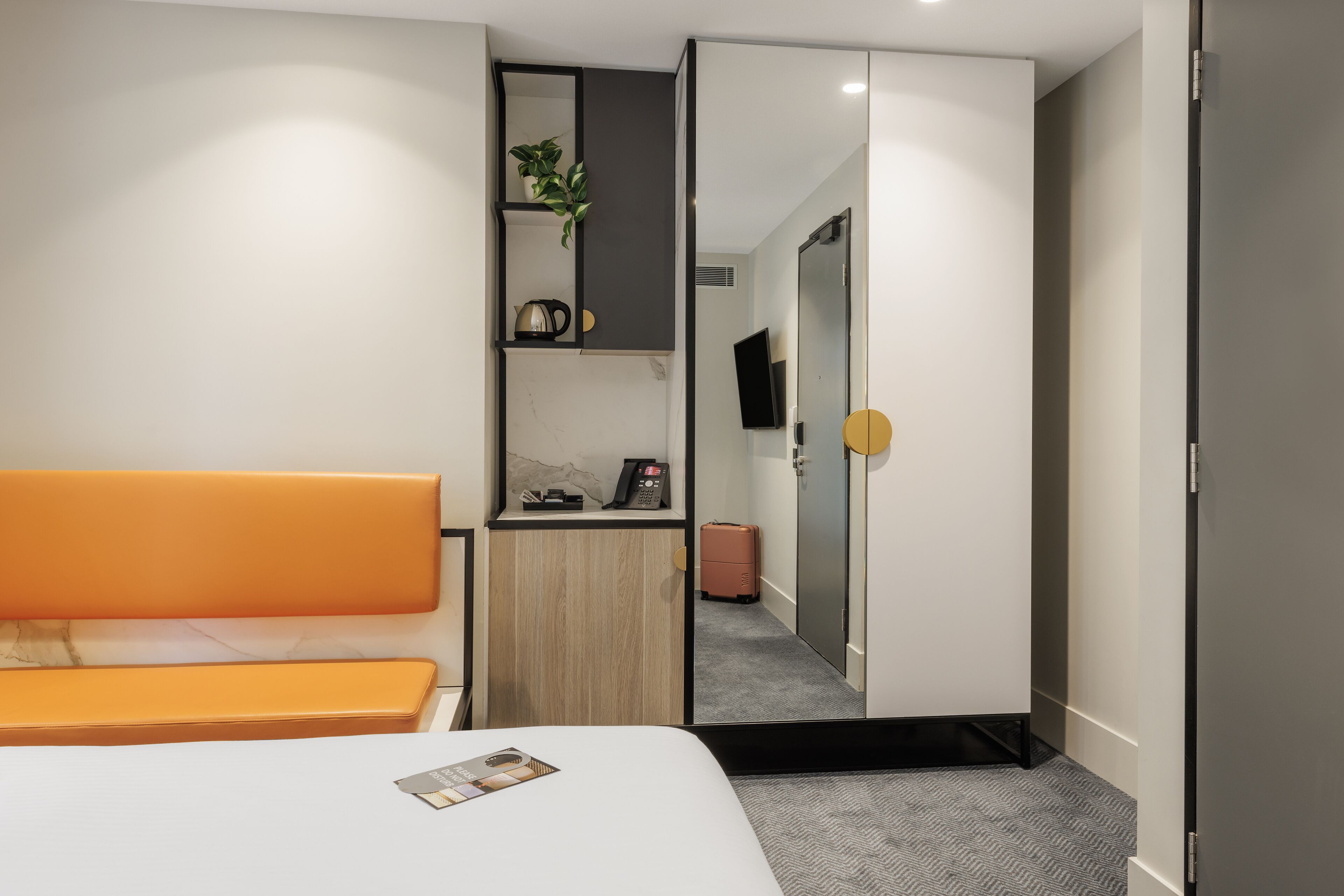 A hotel room with a bed, a desk with a plant, a kettle, and a television.