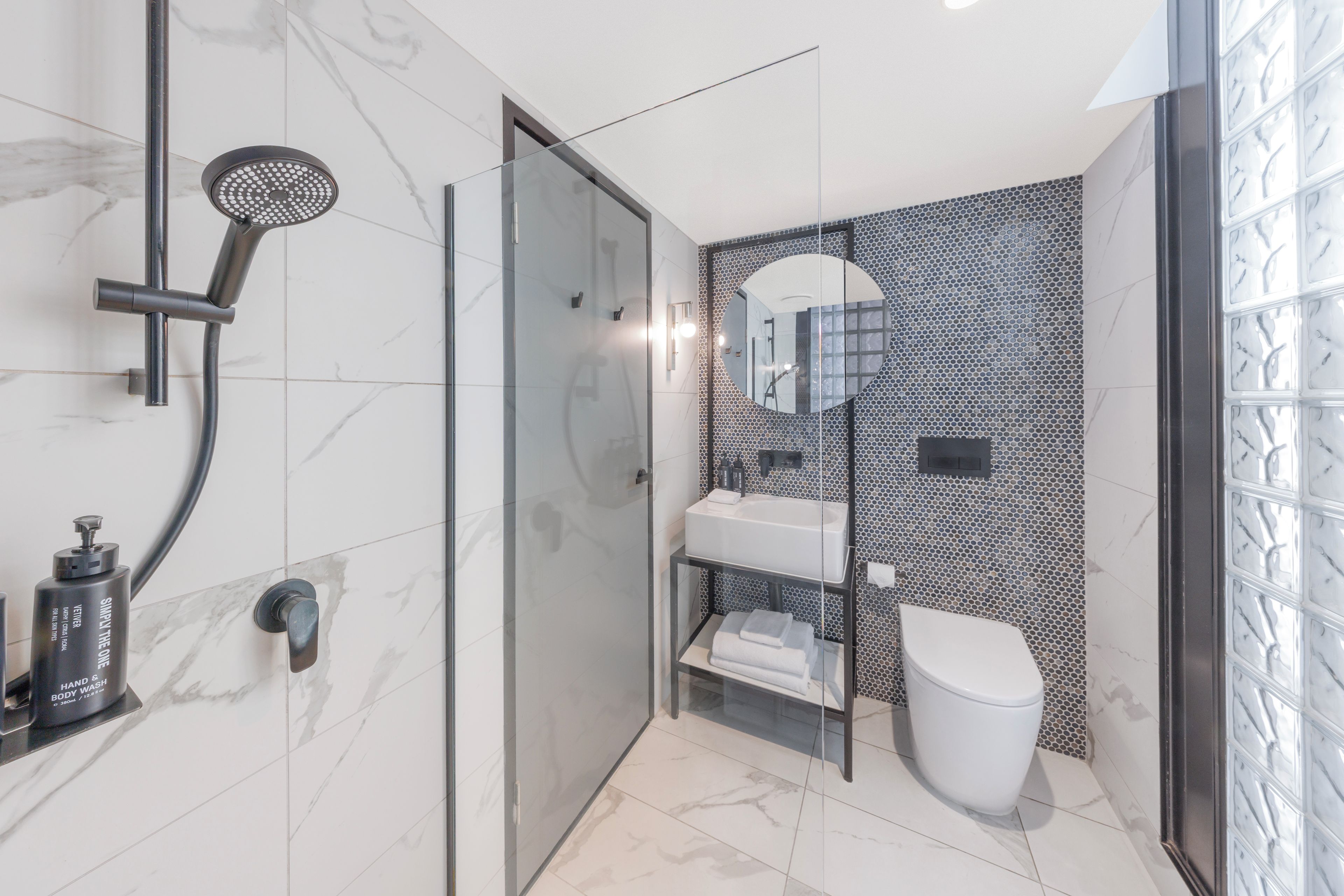 A modern bathroom with a glass-enclosed shower, a white toilet, and a sink with a mirror above it.