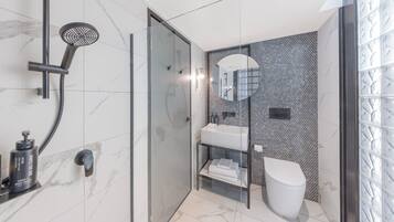 A modern bathroom with a glass-enclosed shower, a white toilet, and a sink with a mirror above it.