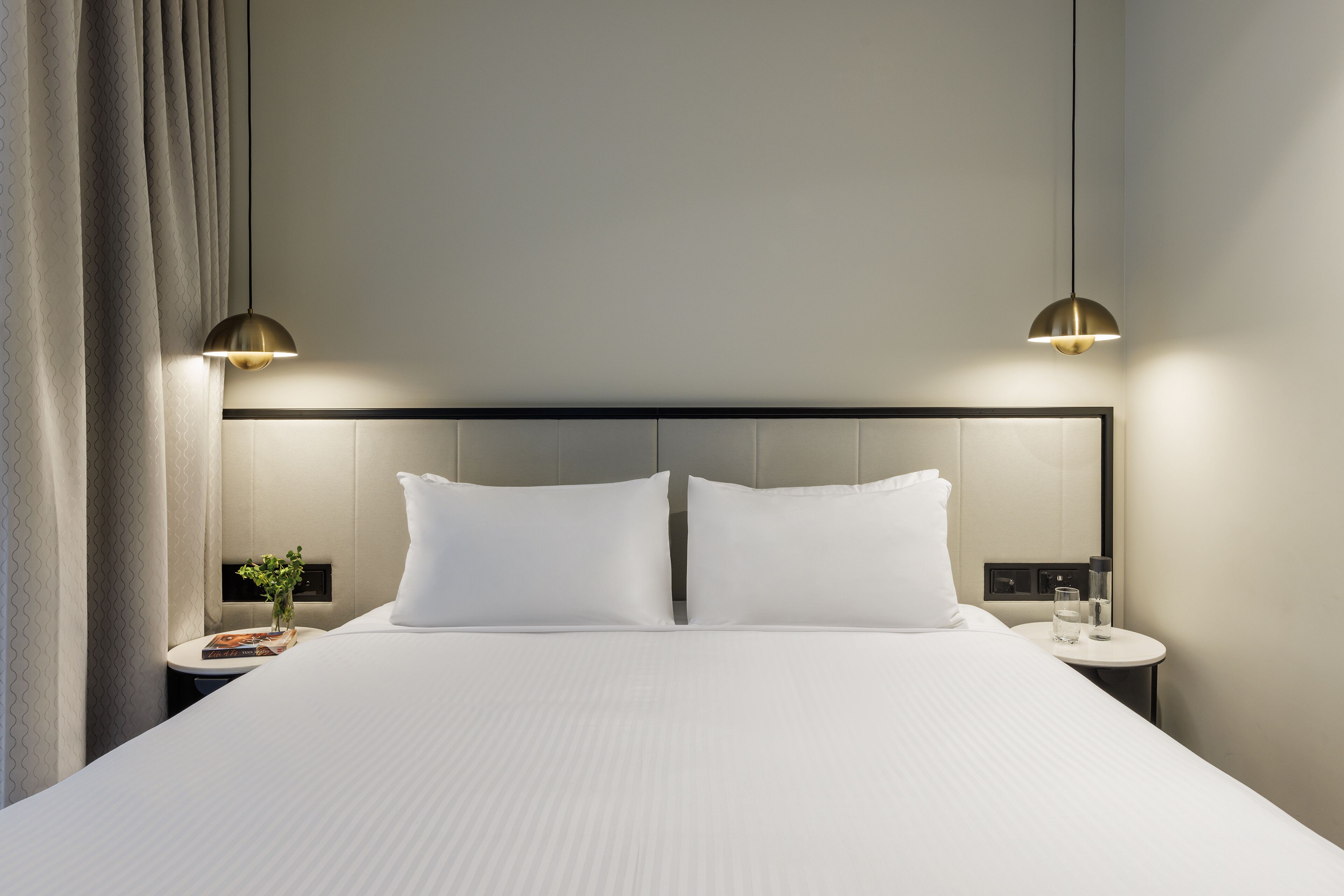 Un lit bien fait, avec du linge de lit blanc, deux tables de chevet avec des lampes et une tête de lit.