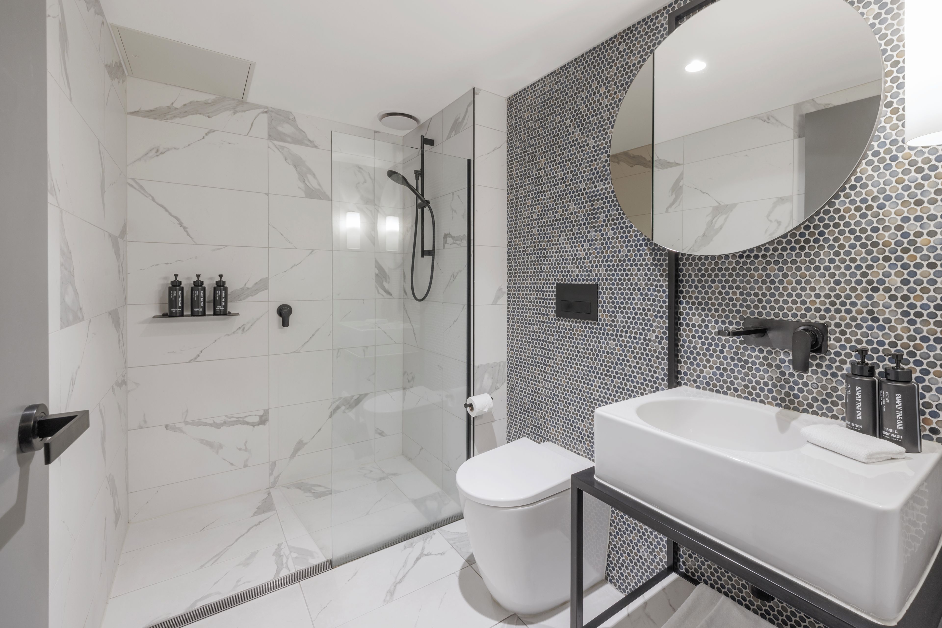 Un baño moderno con ducha envuelta en vidrio, inodoro blanco y lavamanos con espejo.