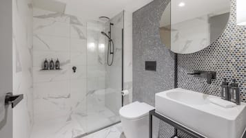 Un baño moderno con ducha envuelta en vidrio, inodoro blanco y lavamanos con espejo.