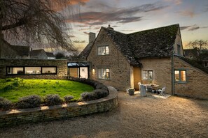 A stone house with a sloped roof, a grassy yard, and a patio with outdoor furniture. - A 5* Star Award winning Cotswold Cottage dating from 1670, with Eco credentials (Southrop)