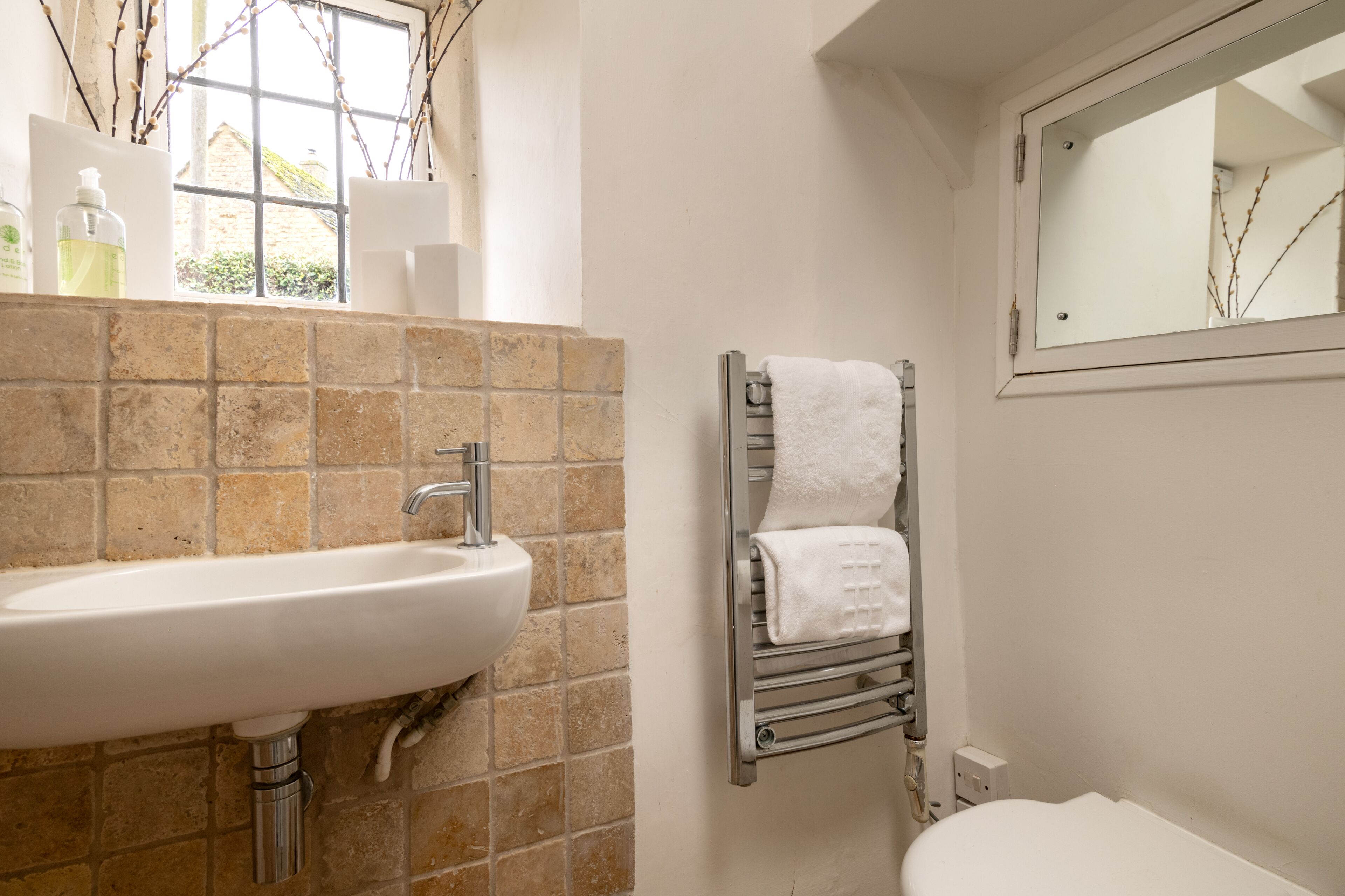 A bathroom with a white sink, a towel rack, and a window with branches.