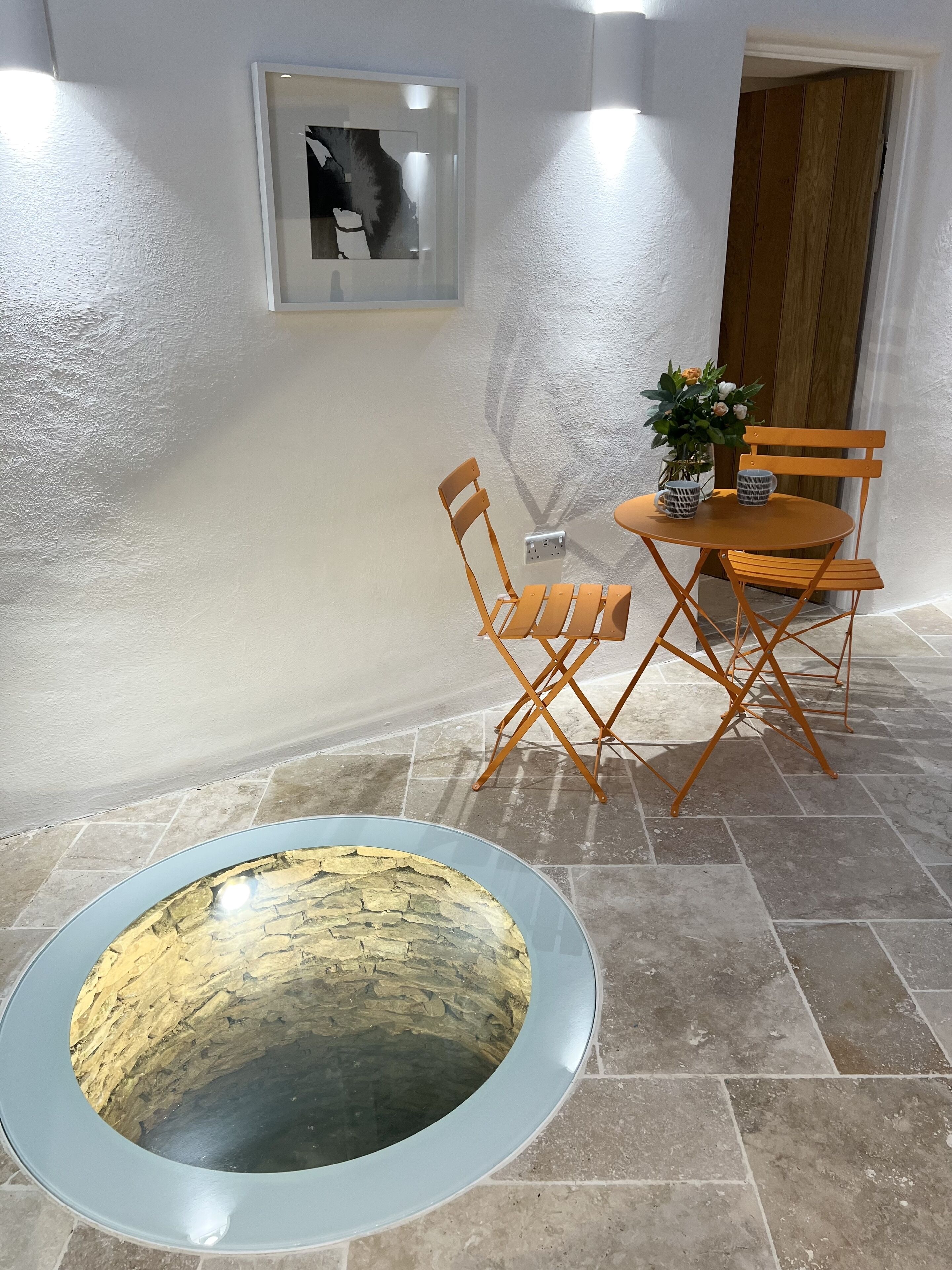 Comedor con una mesa redonda, dos sillas, una planta en maceta y una obra de arte colgada en la pared.