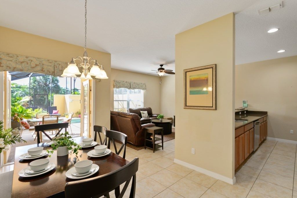 A spacious living area with a dining table set for four, a kitchen with wooden cabinets, and a ceiling fan.