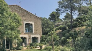 Un edificio de piedra con un amplio ventanal arqueado y un pequeño balcón, rodeado de abundante vegetación y árboles.