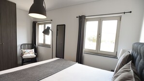Un dormitorio con cama, una silla, un armario, una ventana con cortinas y una lámpara colgante.
