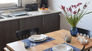 Una cocina moderna con comedor. Incluye un lavamanos, una cafetera y una cesta de frutas. Hay sillas y una mesa listas para comer.