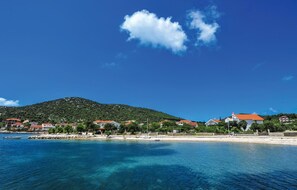 Un paysage côtier avec une eau bleue et limpide, un petit bateau et une colline parsemée de maisons au loin.