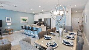 A modern kitchen with white cabinets, a central island, and a dining area with a glass table set for six. - 4BR Townhome in Storey Lake by SHV-4947 (Kissimmee)
