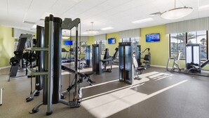 Une salle de sport équipée de divers appareils d’exercice, dotée de grandes fenêtres et d’un téléviseur fixé au mur.