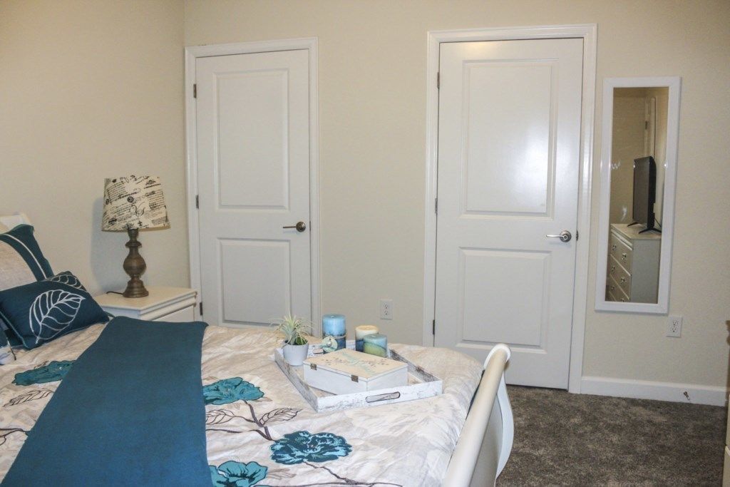 A bedroom with a bed, a nightstand, a lamp, a dresser, and a mirror.