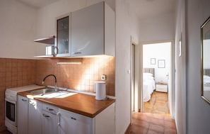 A compact kitchen with a sink, stove, and cabinets, leading to a bedroom with a bed and a bedside table. - 2 bedroom lovely apartment in Vinisce (Vinisce)