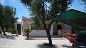 A quiet street with a parked car, a house with a green awning, and a potted plant in the foreground.