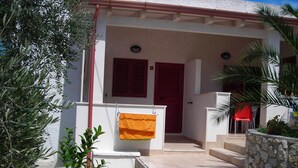 A white building with red shutters, a stone wall, and a tiled entrance.