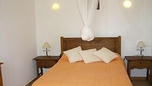 A bedroom with a wooden bed, white pillows, and a canopy. There are two bedside tables with lamps.