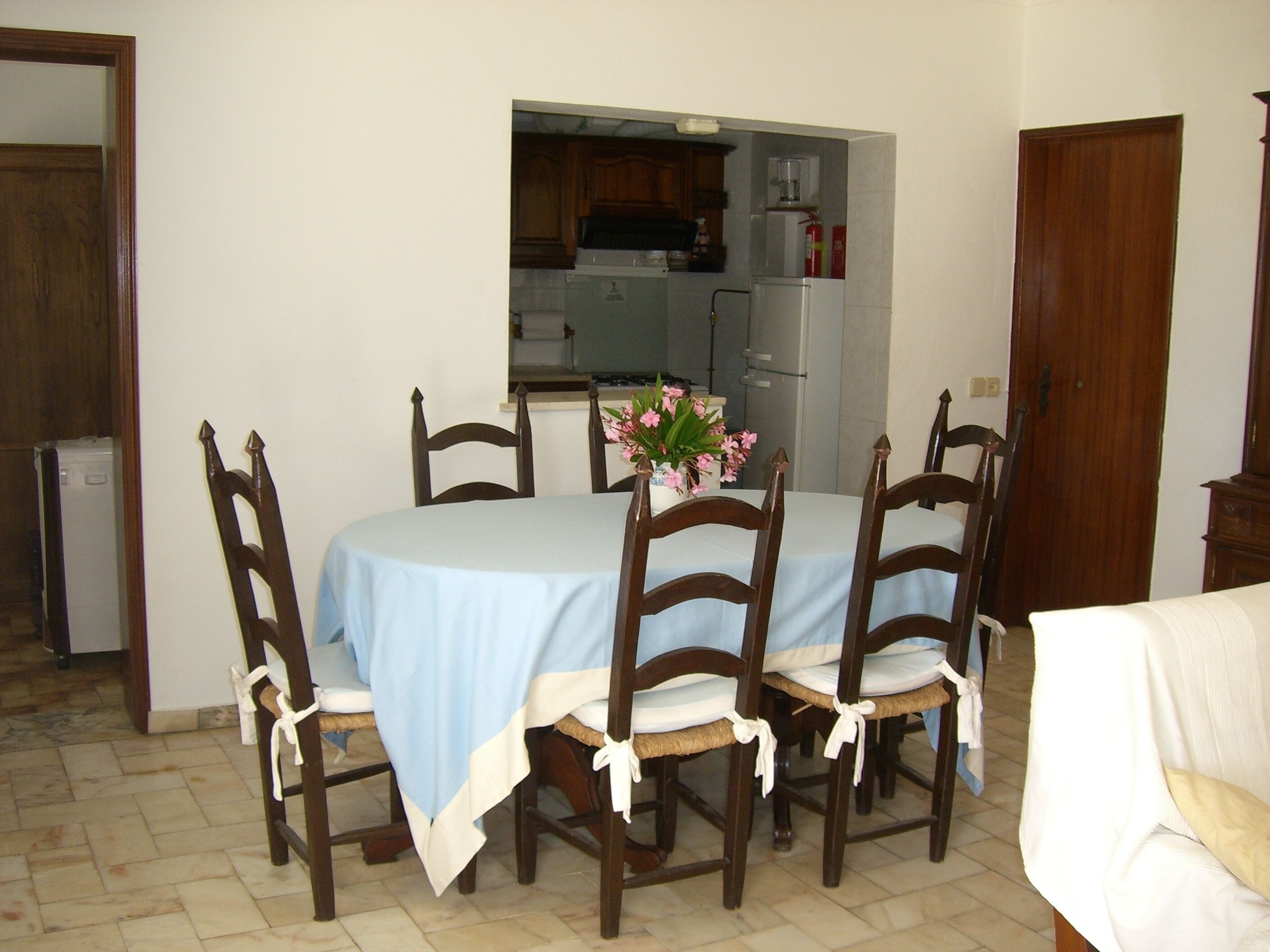 Zona pranzo con tavolo apparecchiato per quattro, circondato da sedie di legno. Sullo sfondo, una piccola cucina.