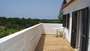 A balcony with a tiled floor, white chairs, and black shutters.