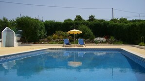 A rectangular swimming pool with a tiled edge, two lounge chairs, and a yellow umbrella.