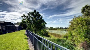 A grassy area with a metal fence, trees, and a pond. - Windsor Hills 2nd Premium 5/5 Lake View Home w/South Pool-Near Disney (Kissimmee)