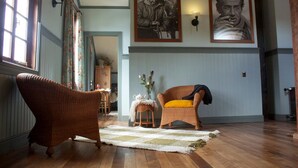 A room with a wooden floor, two wicker chairs, a small table with a vase, and a large painting on the wall. - Estancia 440 Hotel Boutique (Puerto Varas)
