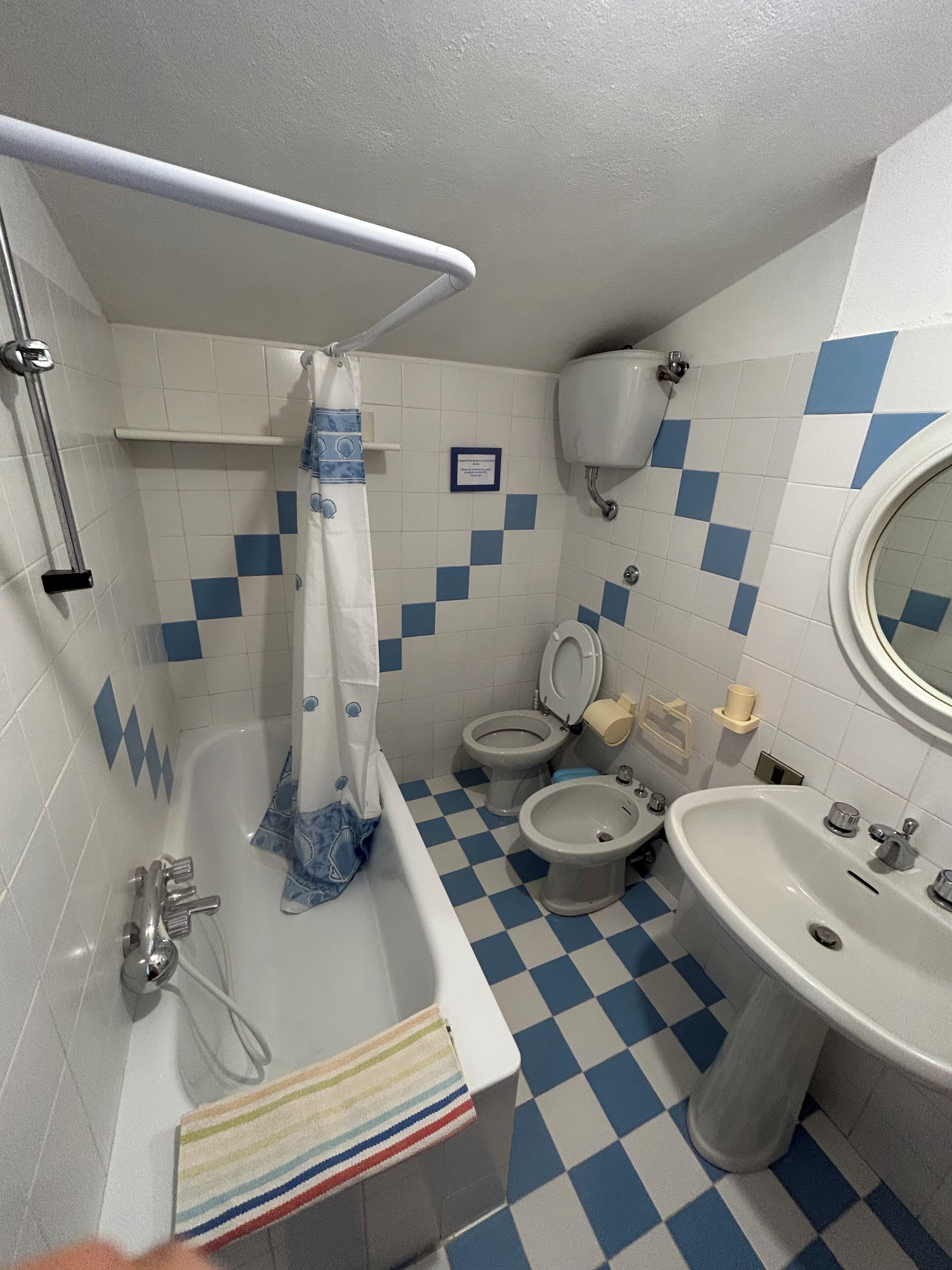 Ein Badezimmer mit Schachbrettboden, zwei Toiletten, einer Badewanne und einem Waschbecken.