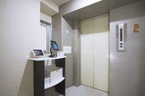 An elevator with a control panel and a digital display, a door with a number 2 sign, and a small kiosk with a screen and a box.