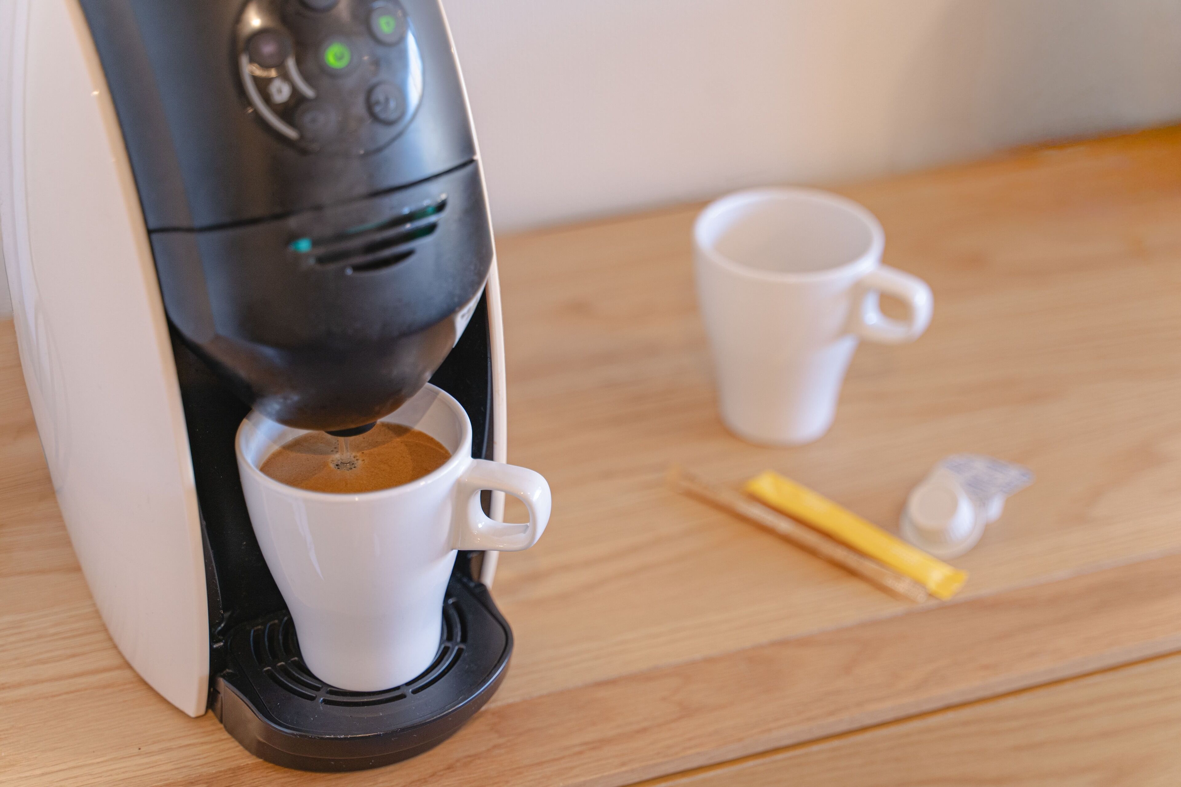 Eine Kaffeemaschine auf einem Holztisch, mit einer weißen Tasse und einem gelben Gegenstand in der Nähe.