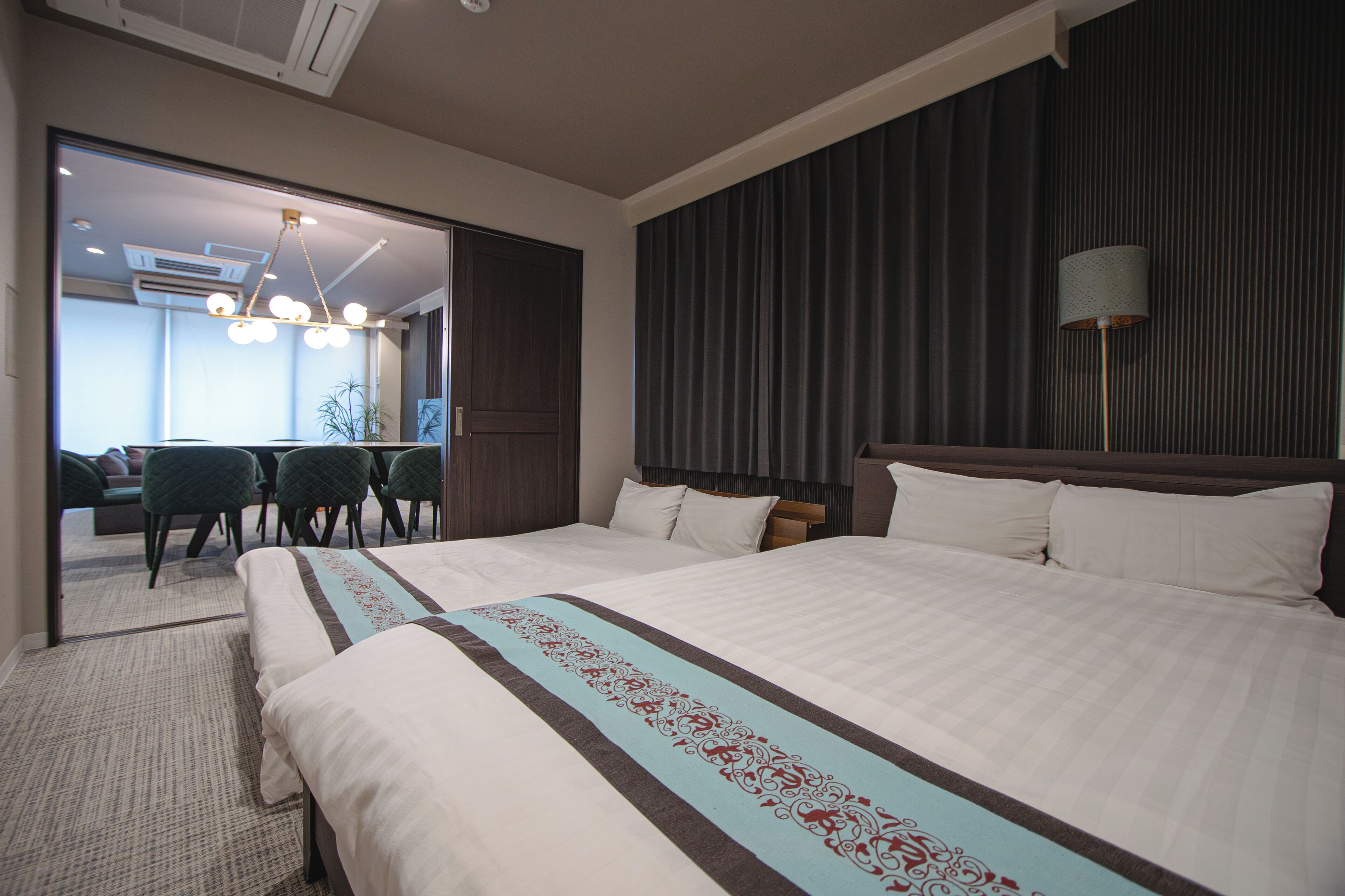 A hotel room with a large bed, a desk with chairs, a mirror, and a dark-colored headboard.