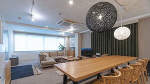 A modern living room with a wooden dining table, comfortable seating, a large window, and a decorative spherical light fixture. - INOVE VILLA OSAKA (Osaka)