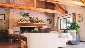 A spacious living room with a brick fireplace, wooden beams, and a large window. - María & Bernardo Casa - Viñedo (El Marques)