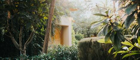 A lush garden with a wooden structure surrounded by dense foliage and a large hay bale.