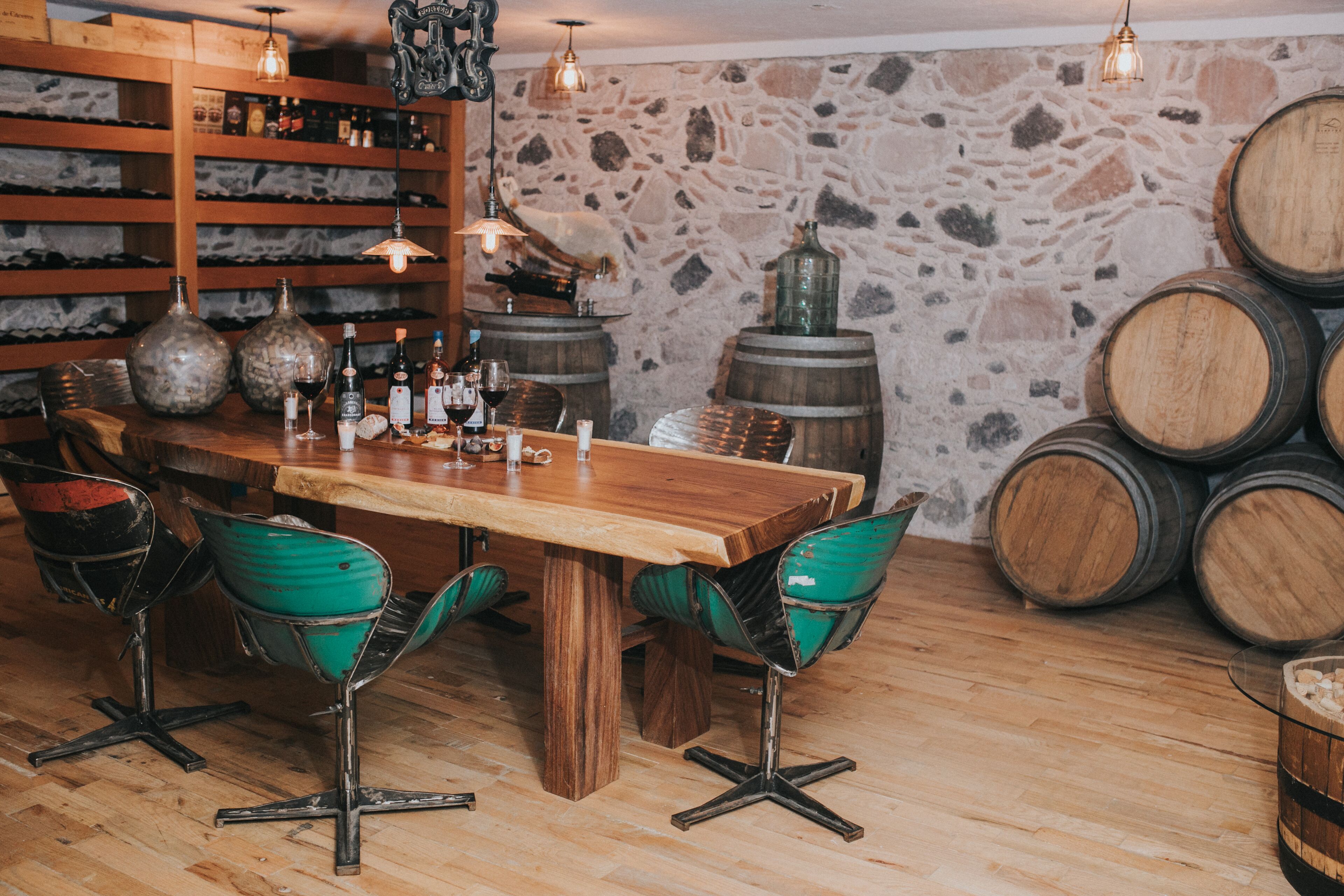 A rustic bar area with wooden furniture, stone walls, and wine barrels.