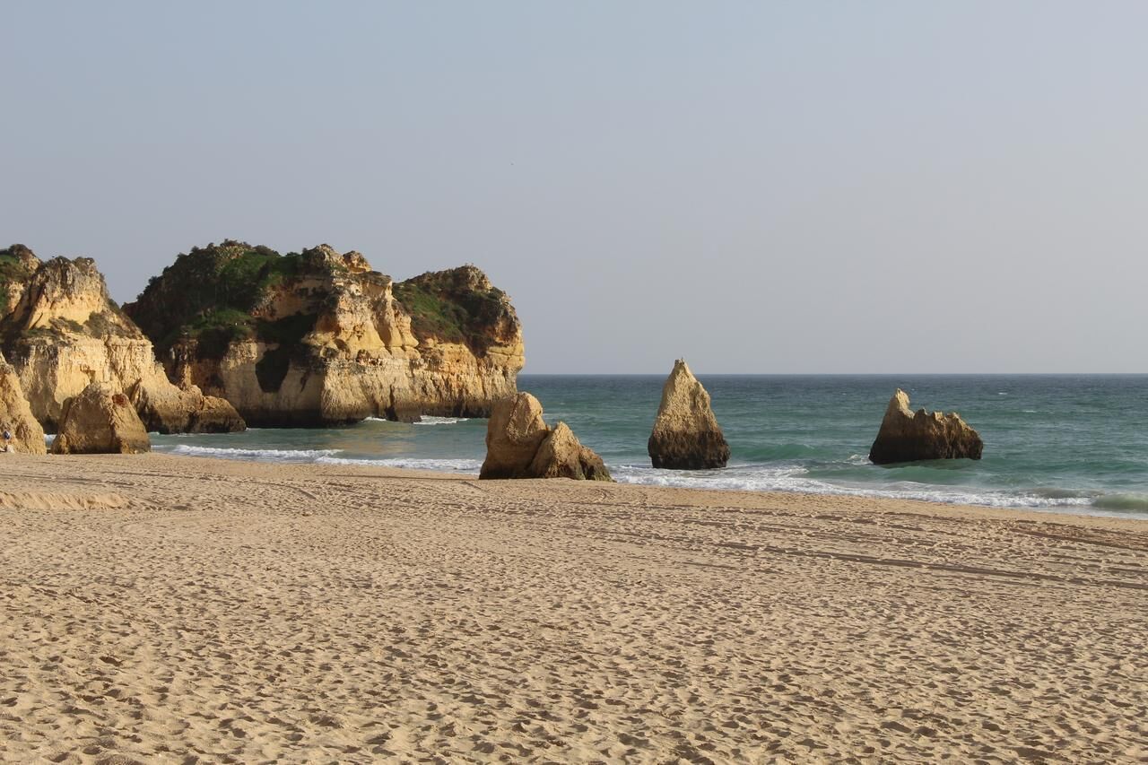 A sandy beach with large rock formations and a clear sky.