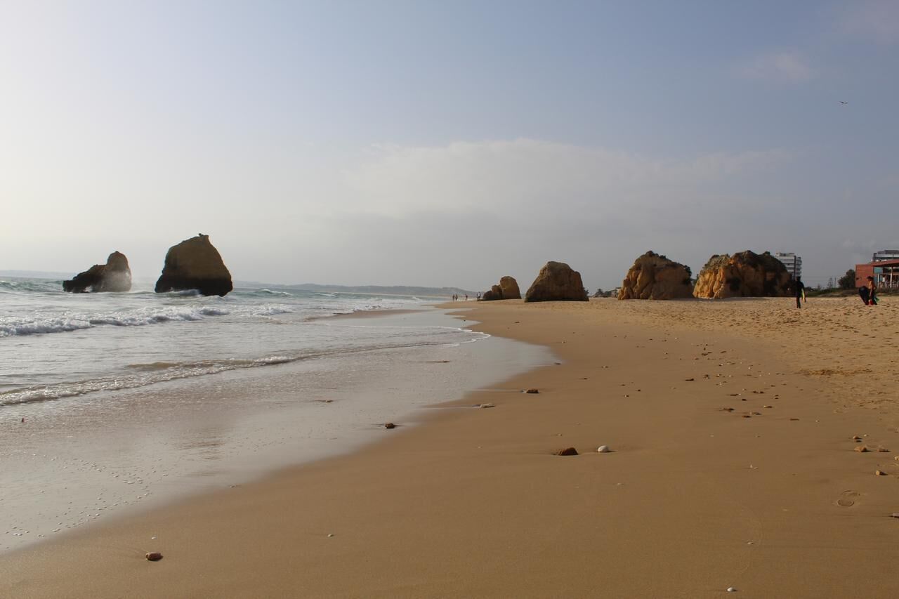 Ein sandiger Strand mit großen Felsformationen und einem klaren Himmel.
