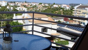 Un balcone con un tavolo rotondo e una lanterna decorativa, affacciato su una zona residenziale con edifici e pannelli solari.
