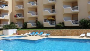 Una piscina con lettini, un muro in pietra e un edificio a più piani con balconi.