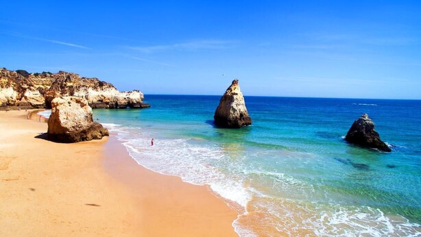 Una spiaggia con acque cristalline turchesi, una costa sabbiosa e formazioni rocciose.