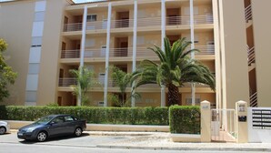 Un palazzo a più piani con balconi, un ingresso con cancello e palme.