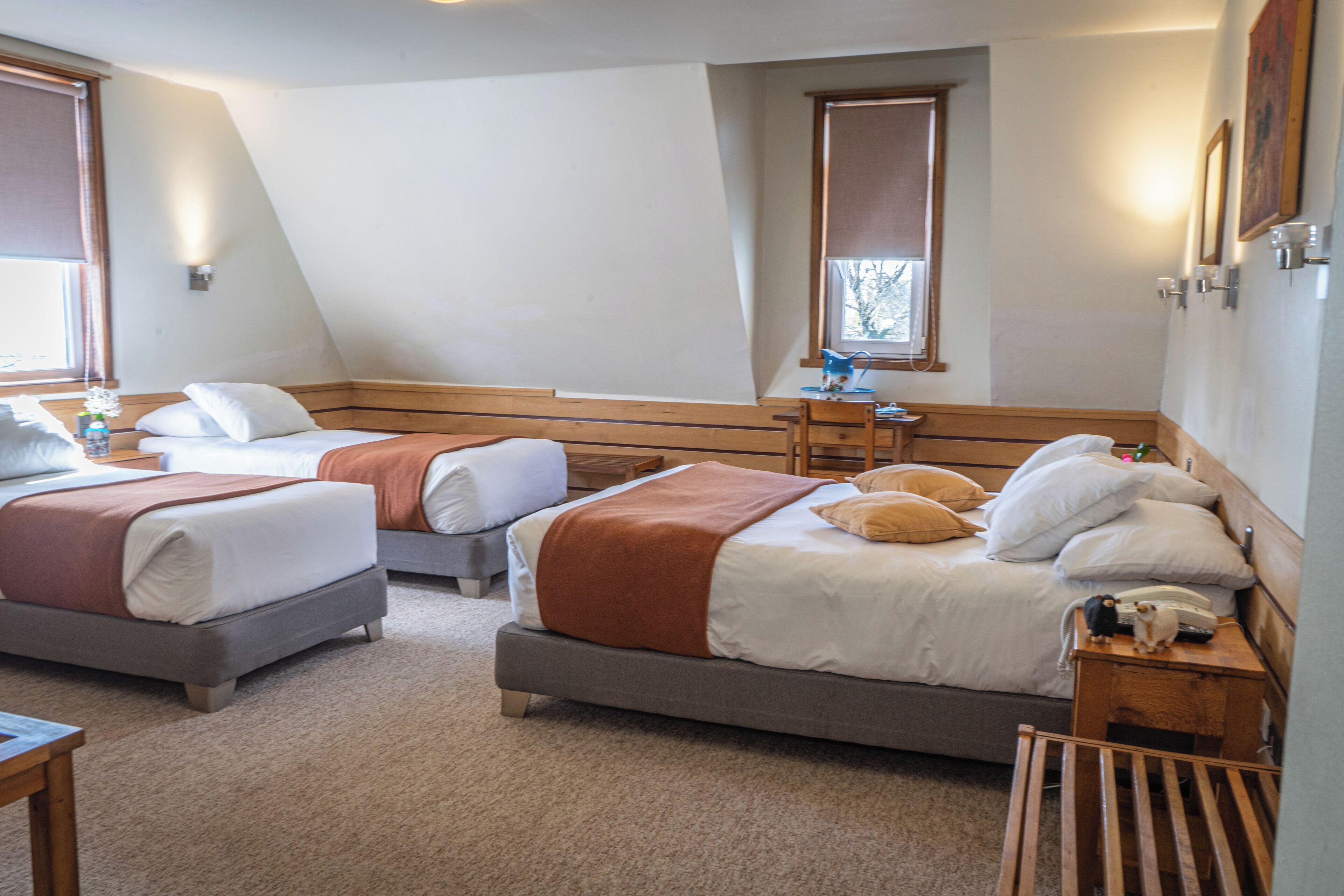 Ein Hotelzimmer mit zwei Betten, einem hölzernen Kopfteil, einem Nachttisch mit Lampe und einem Fenster mit Jalousien.