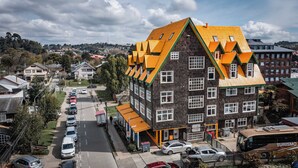 A multi-story building with a distinctive yellow roof and stone facade, located in a residential area with parked cars and a bus.