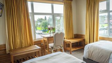 Une chambre d’hôtel avec deux lits, un bureau et une chaise. Il y a une fenêtre avec des rideaux, et la chambre offre une vue sur l’extérieur.