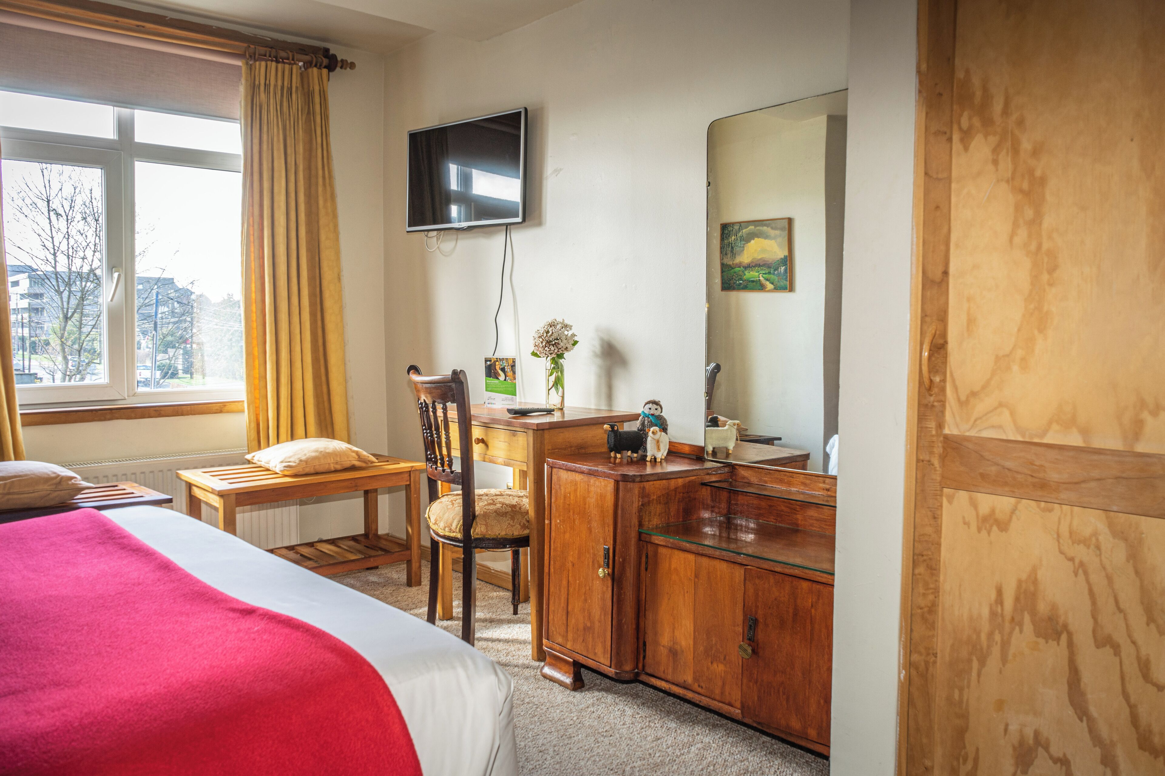A hotel room with a bed, a desk, a chair, a television, a mirror, and a window with curtains.