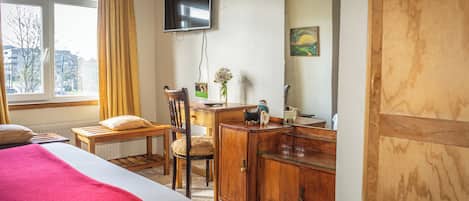 A hotel room with a bed, a desk, a chair, a television, a mirror, and a window with curtains.