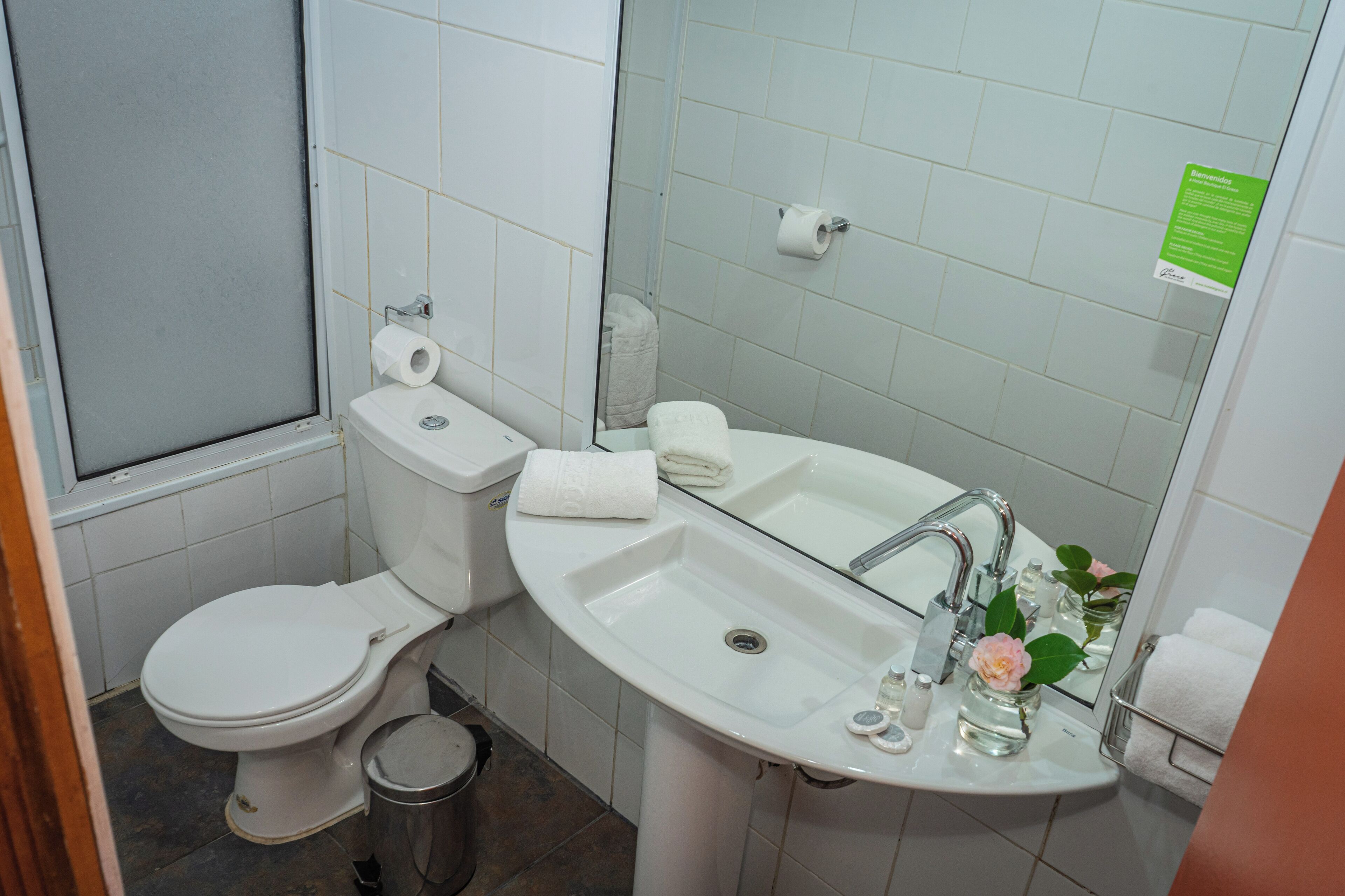 Un bagno con il water, un lavandino e uno specchio. Si nota anche un cestino e un portasciugamani.
