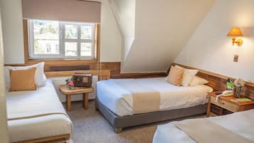 A bedroom with two beds, a window with a view, a bedside table with a lamp, and a small table with a radio.